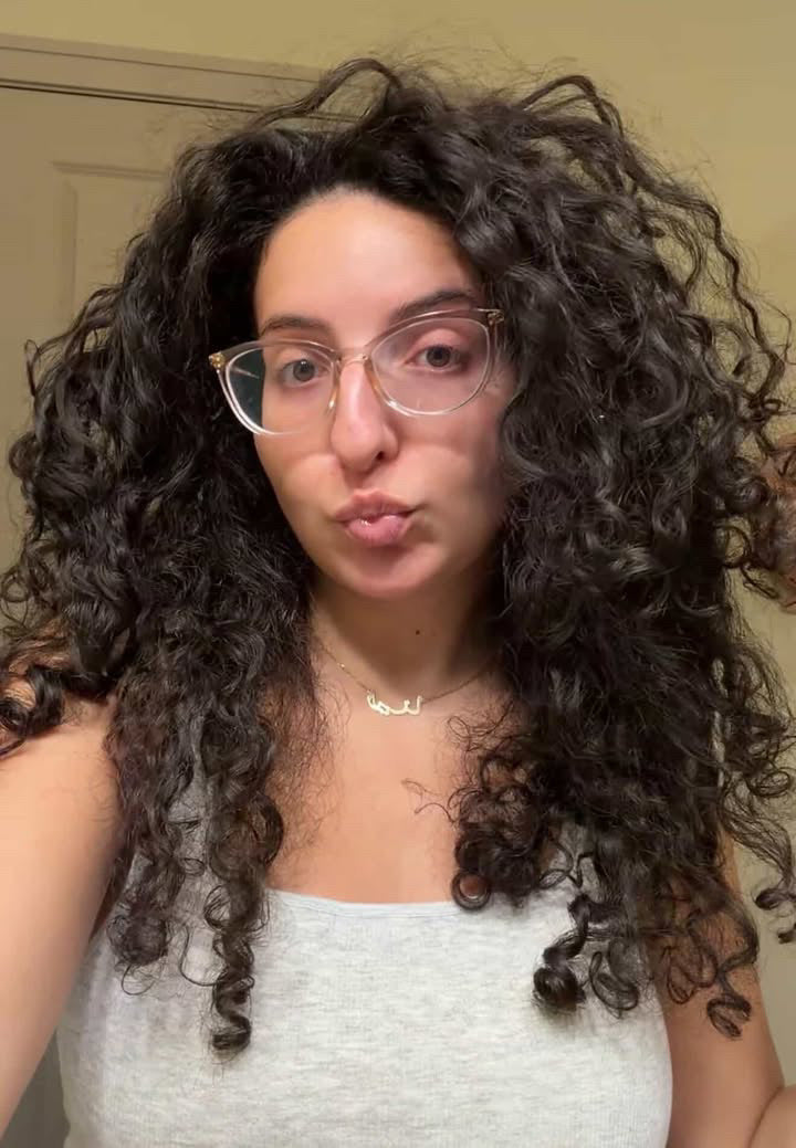 Person with curly hair and glasses making a duck face in front of a neutral background