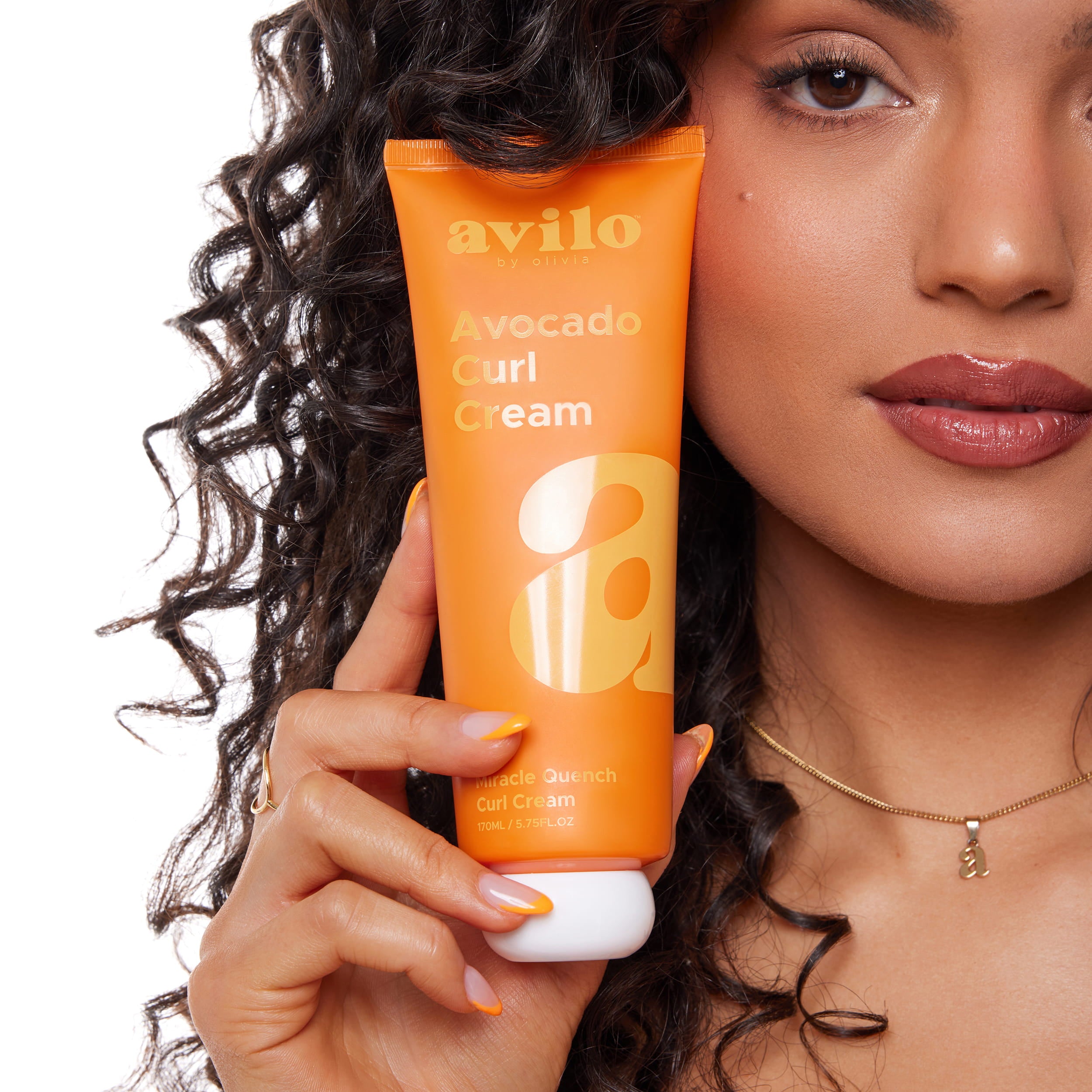Woman holding an orange tube of Avilo Avocado Curl Cream with her hair.