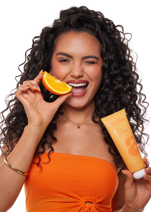 Woman holding an orange and a tube of sunscreen with a white background