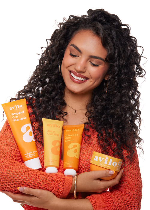 Woman holding Avilo hair care products against a white background

