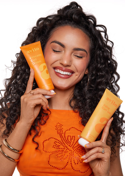 Woman holding two orange bottles of Avito sunscreen with a white background