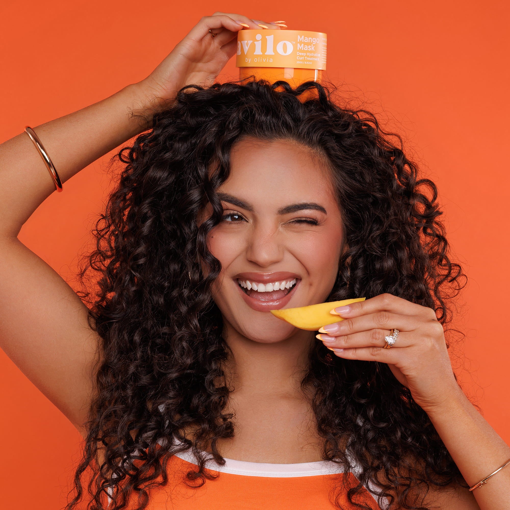 Woman with curly hair holding a container of 'vilo' product against an orange background