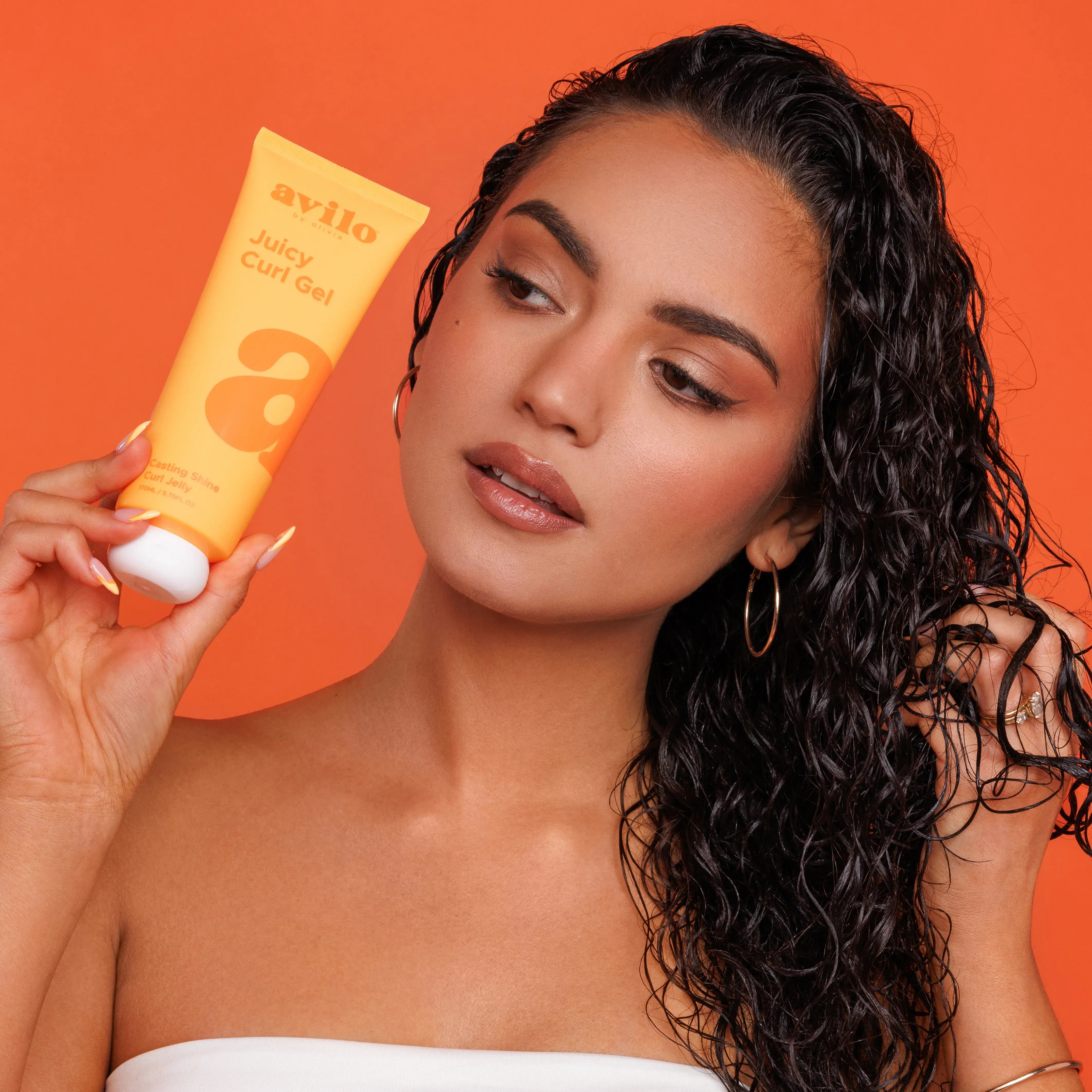 Woman holding an Avlio Juicy Curl Gel against an orange background