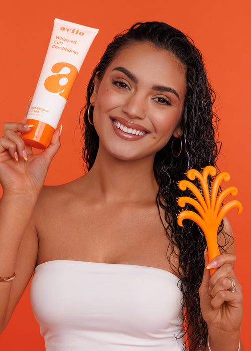 Woman holding a bottle of Avlon hair care product and a brush against an orange background