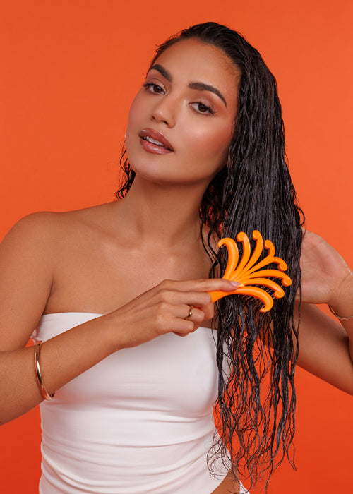 Woman with wet hair holding an orange hairbrush against an orange background
