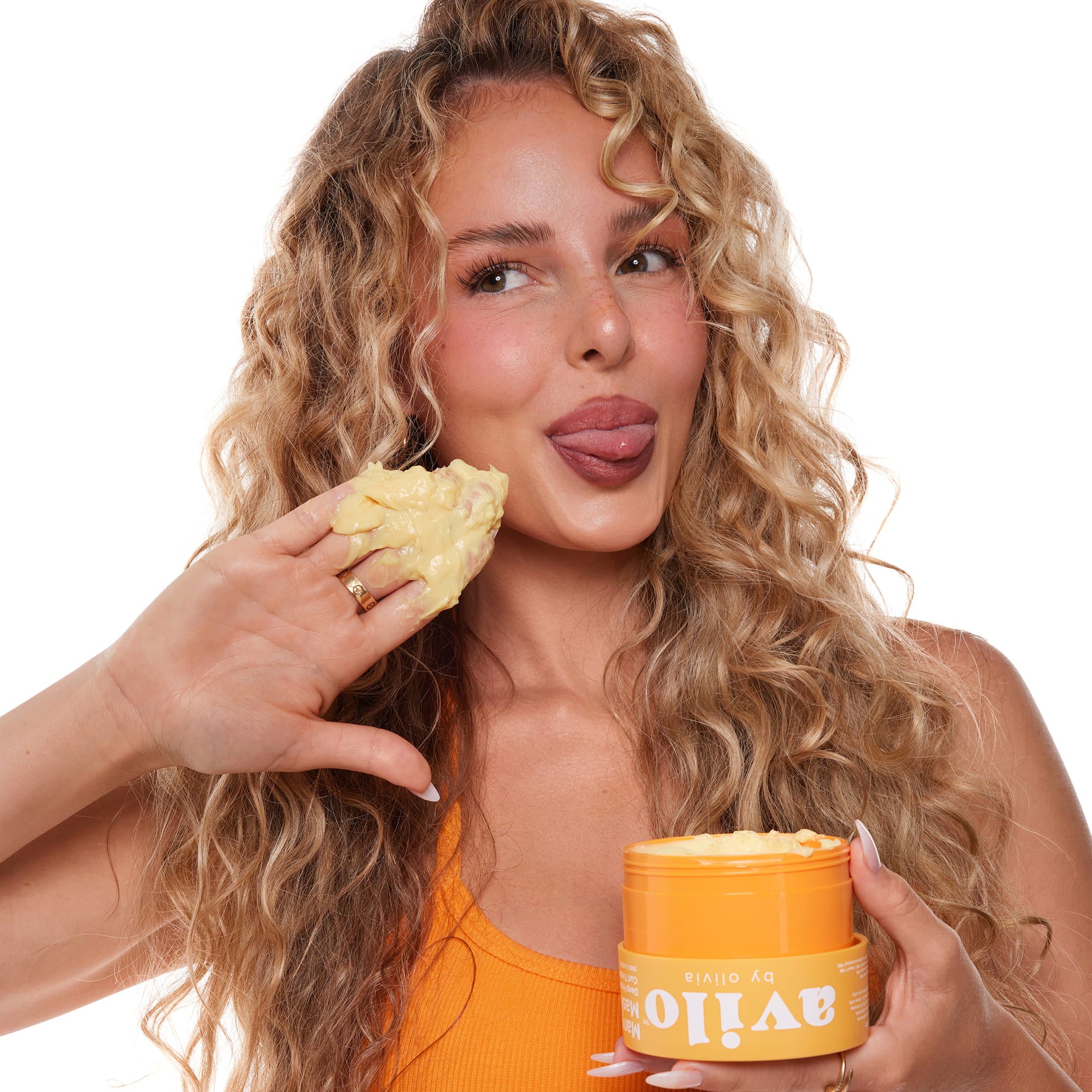 Woman with curly hair holding a container of hair product and a small amount of product in her hand on a white background