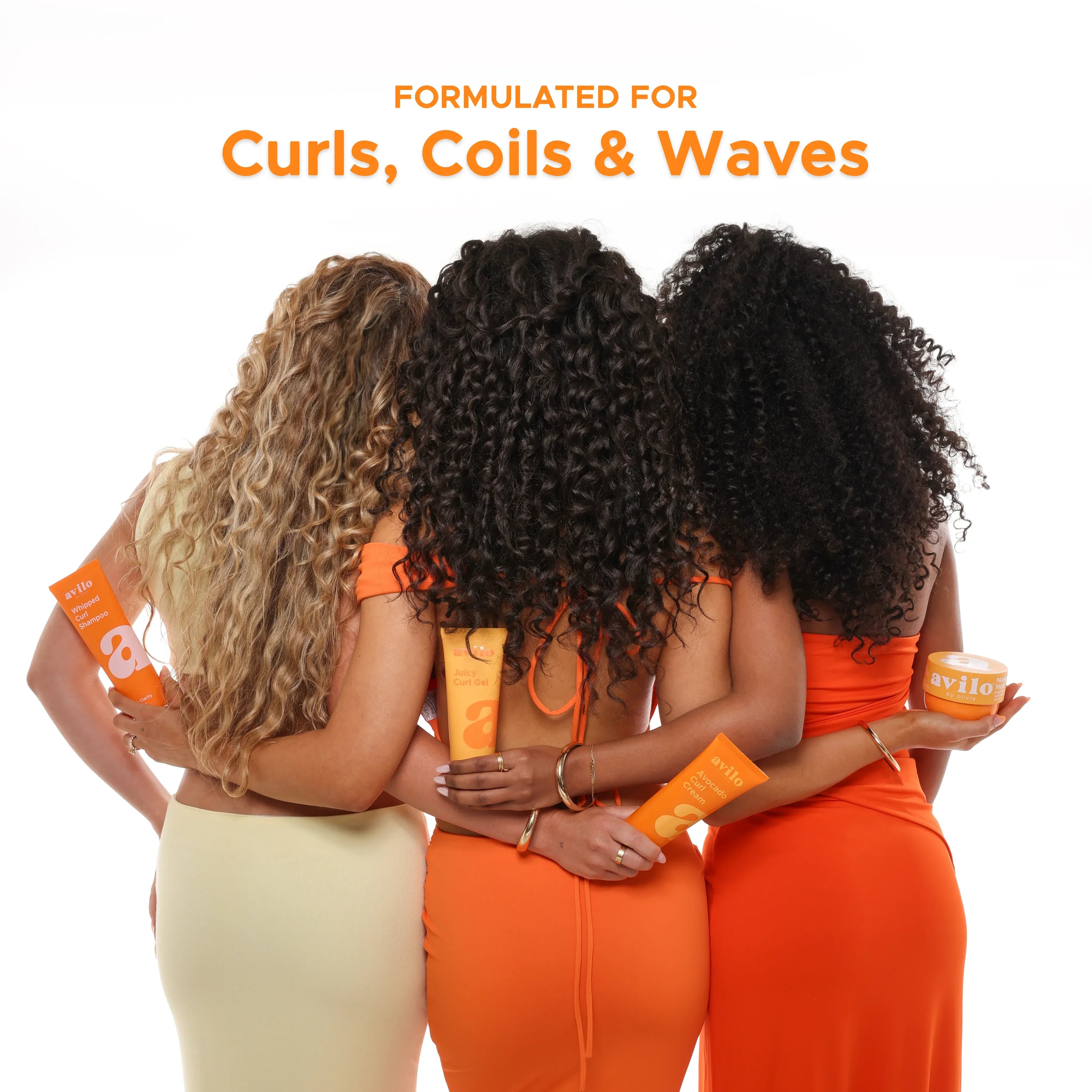 Three women with curly hair embracing, holding orange products, with text 'Formulated for Curls, Coils & Waves' above.

