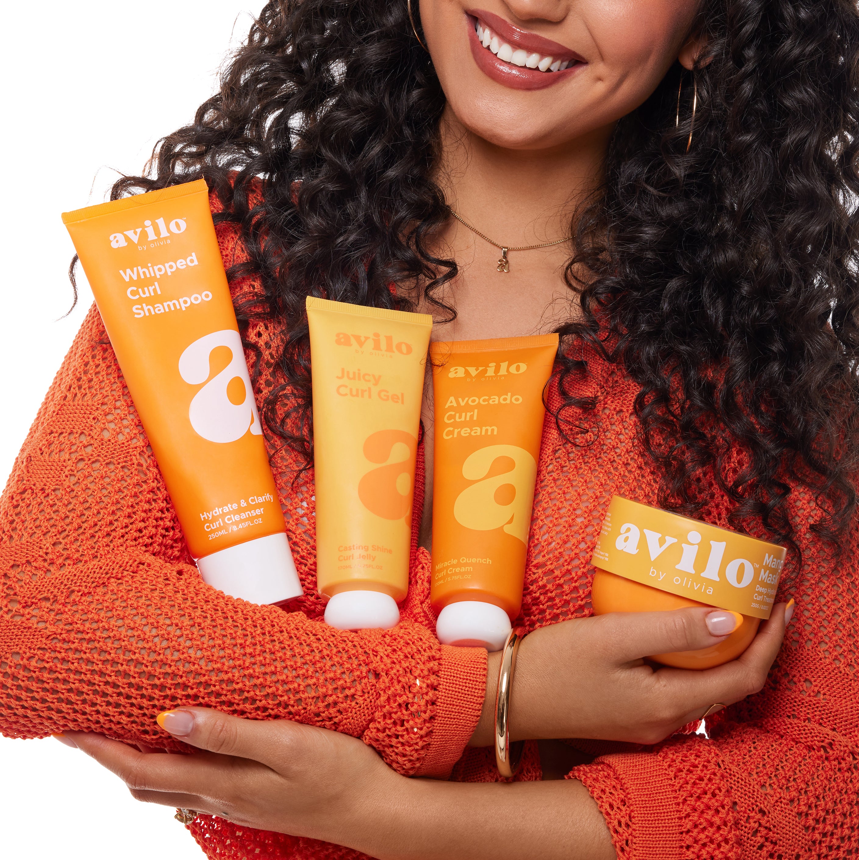 Woman holding avilo hair care products against a white background