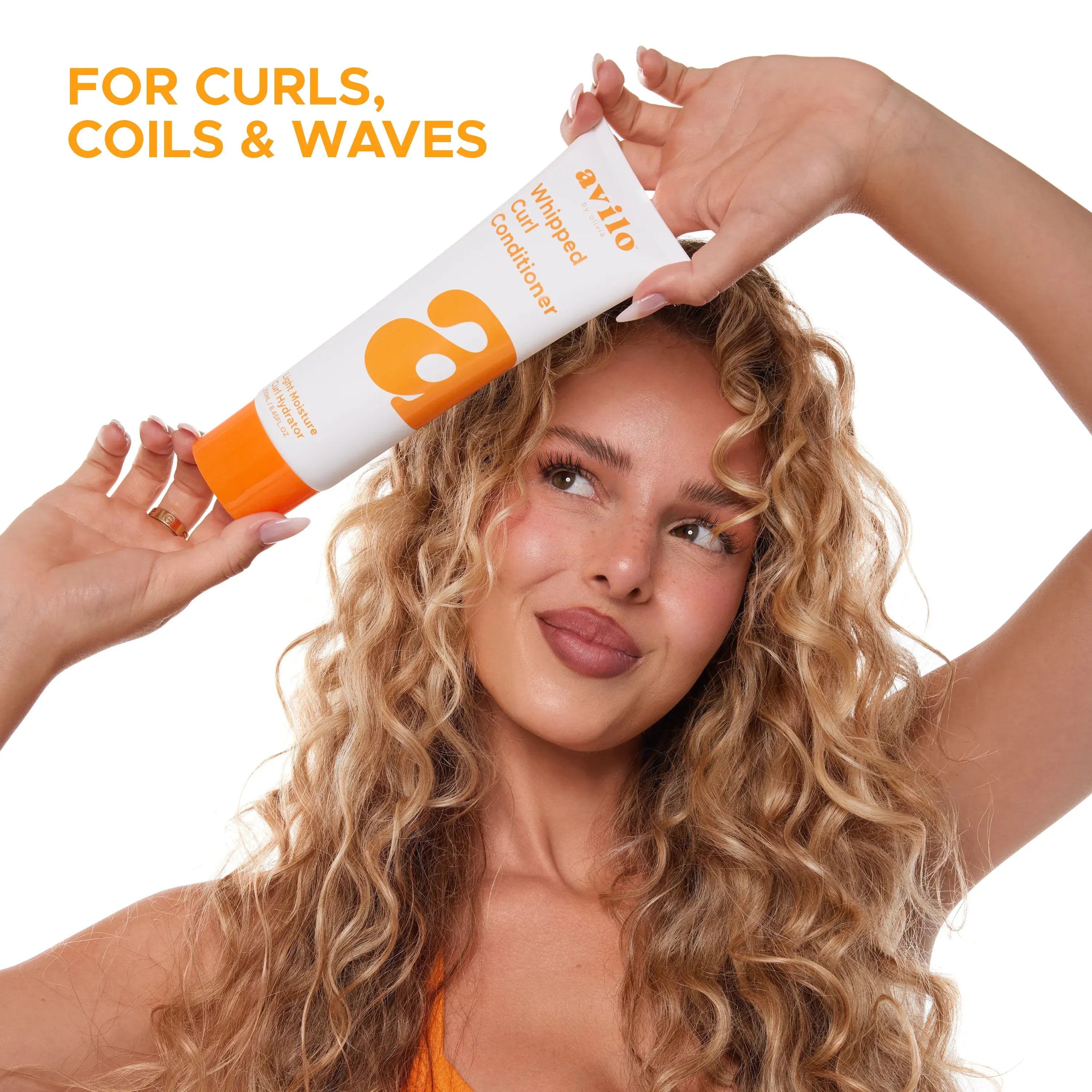 Woman with curly hair holding a tube of hair product with text 'For Curls, Coils & Waves