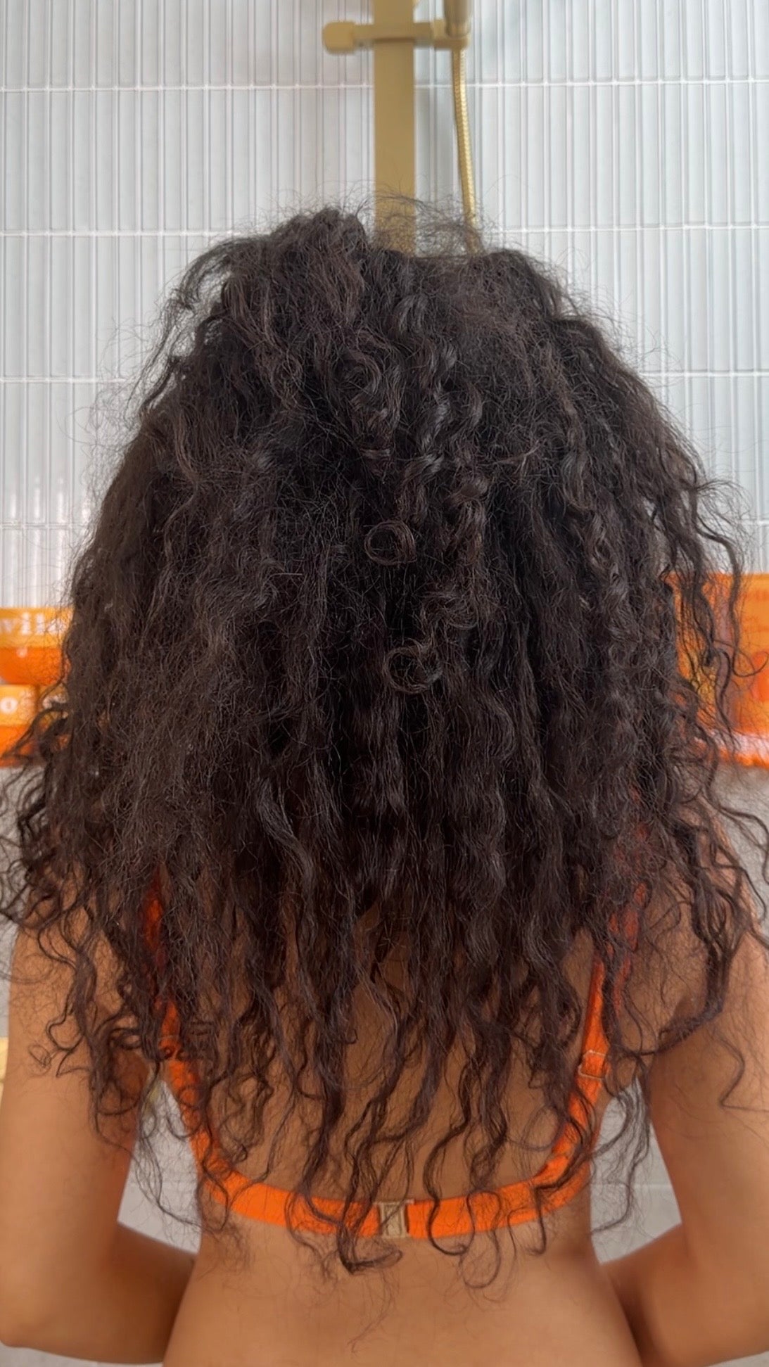 Person with curly hair wearing an orange bikini top in a bathroom setting.
