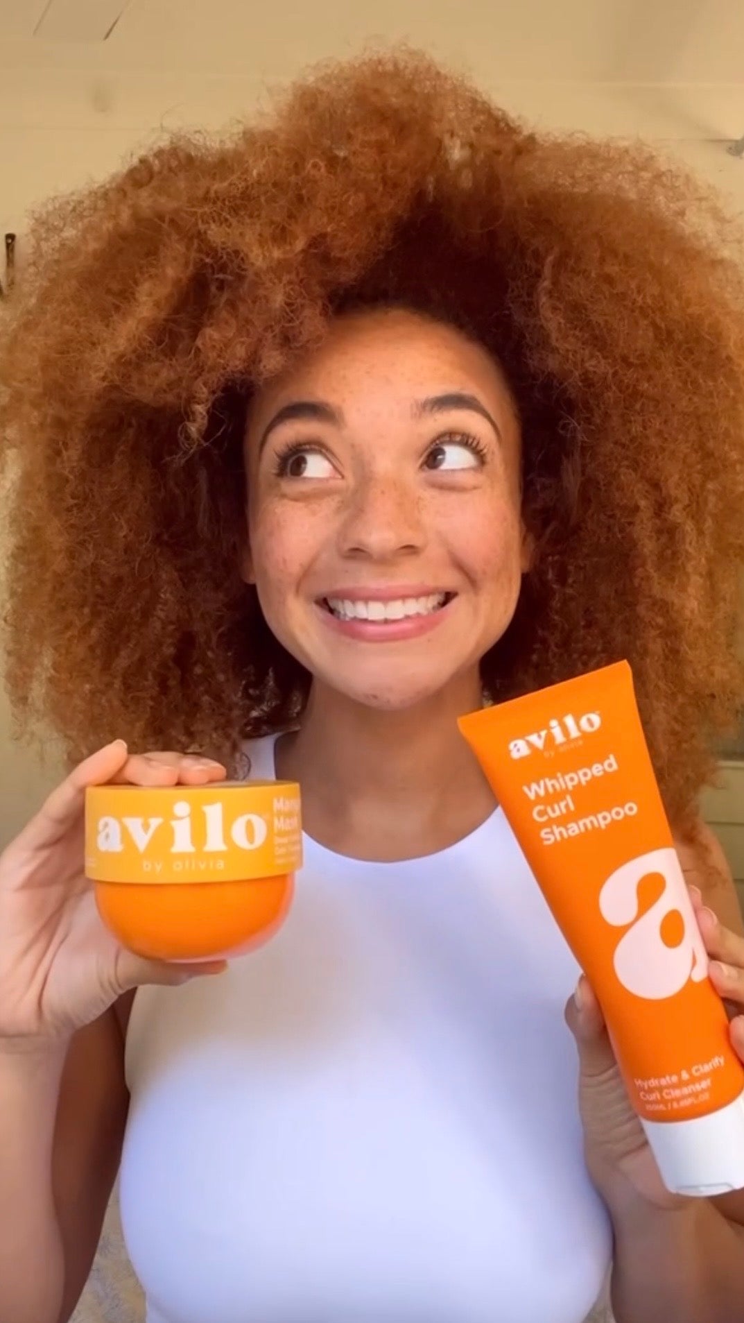 Woman holding Avilo whipped curl shampoo and a bowl, smiling.
