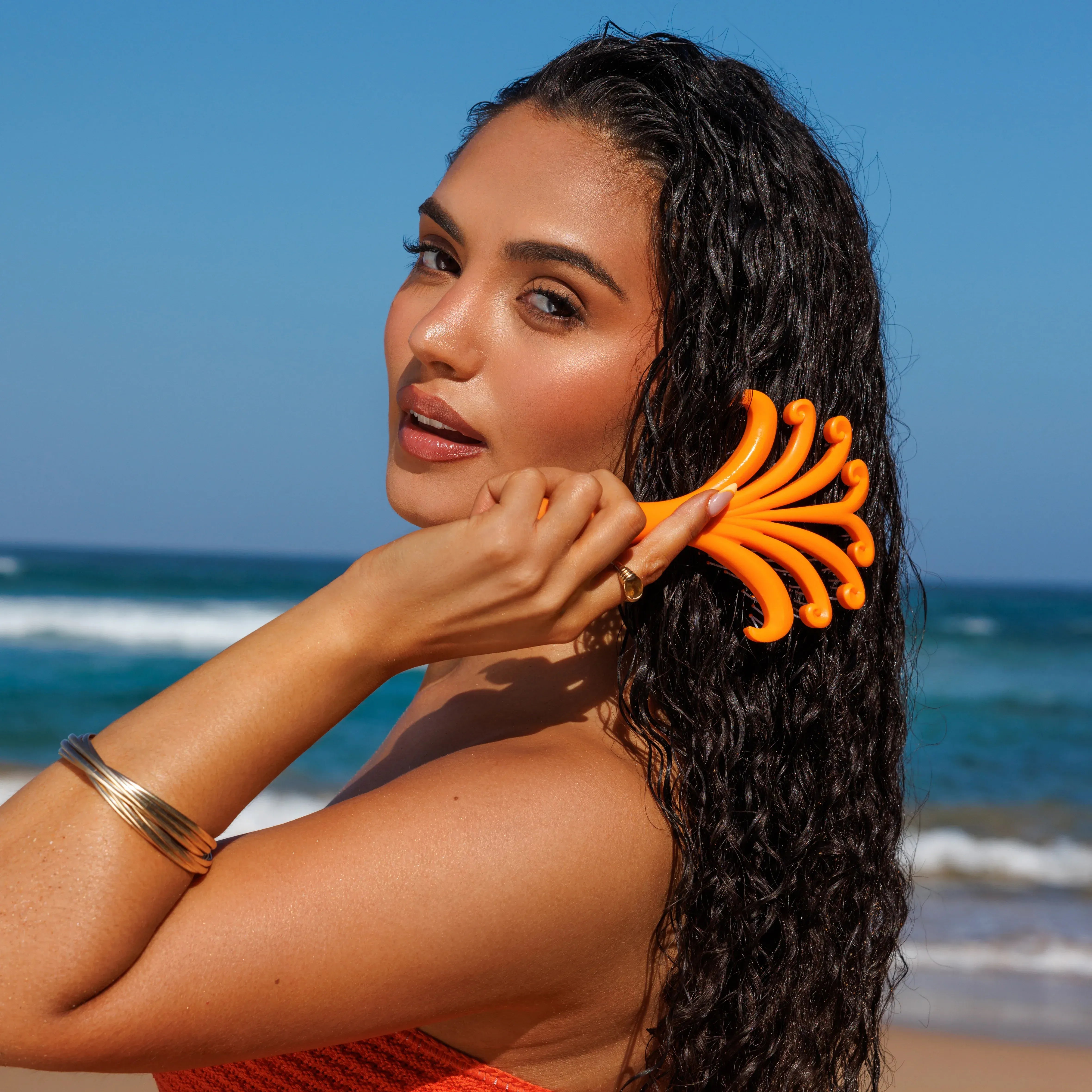 Woman brushing her hair with an orange brush on a beach