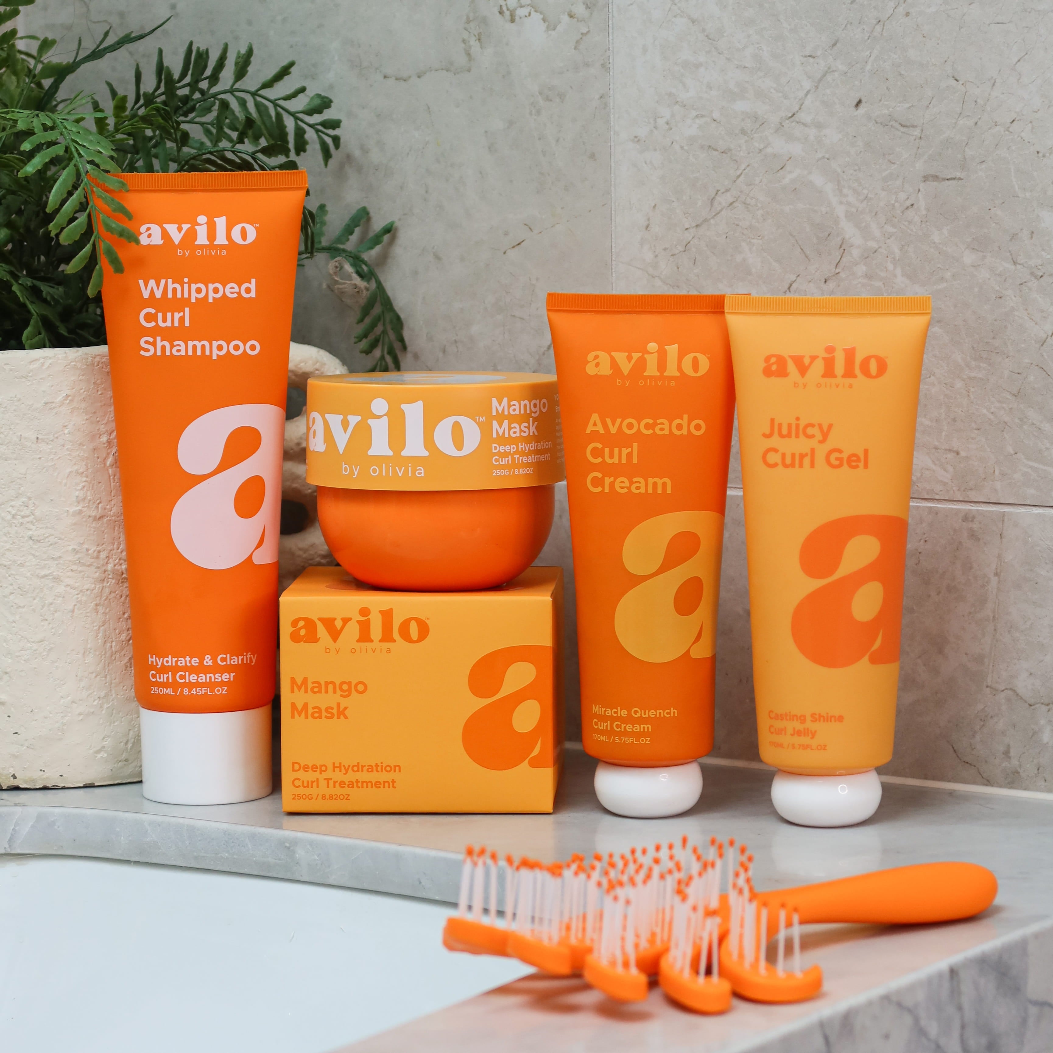 Avilo hair care products including shampoo, mask, cream, and gel on a bathroom shelf.


