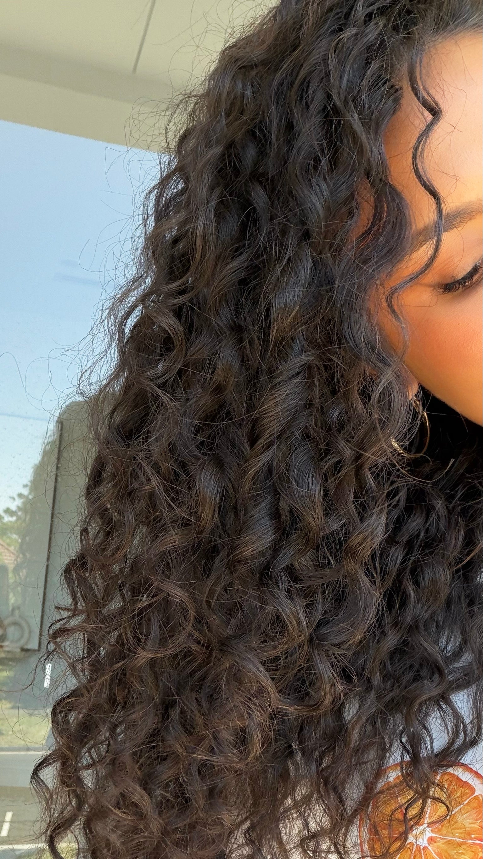 Close-up of a person with curly hair, outdoors.

