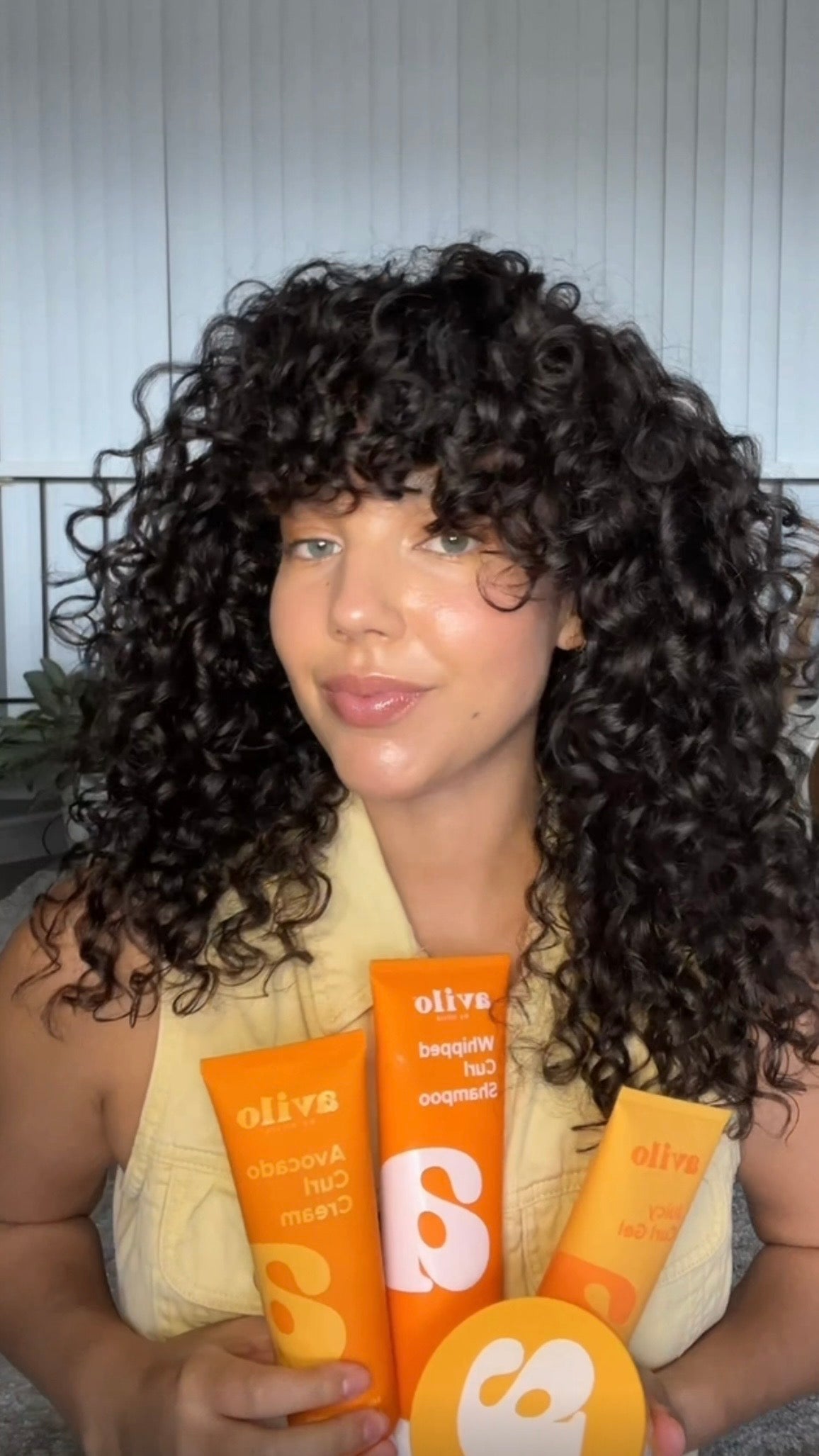 Woman holding orange hair care products with a neutral background

