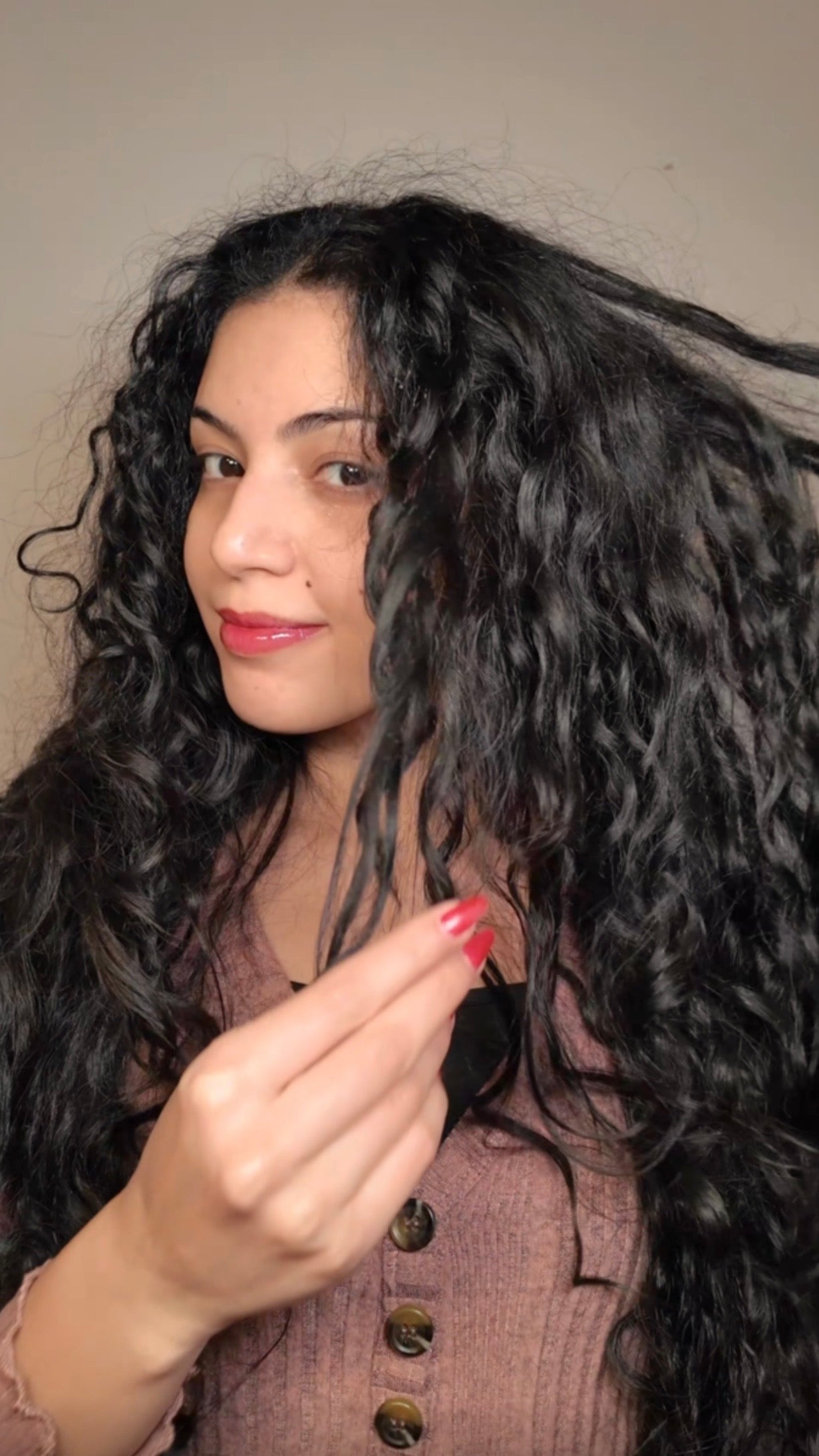 Woman with long, dark hair holding a section of it in front of a neutral background