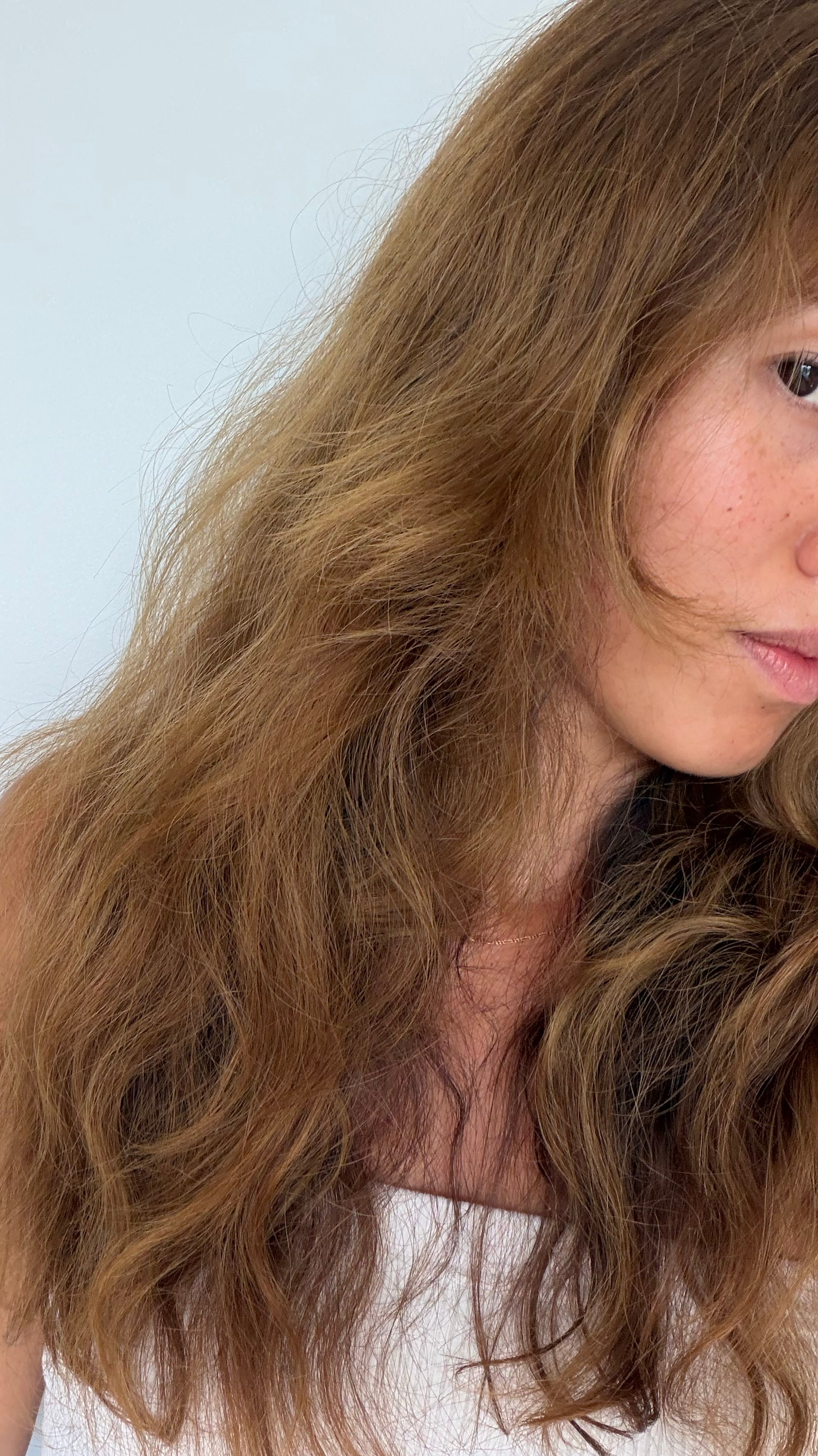 Close-up of a person with wavy brown hair against a light background

